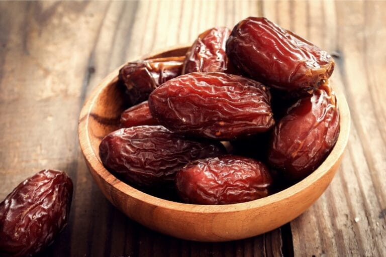 A wooden bowl filled with fresh Medjool dates resting on a rustic wooden surface.